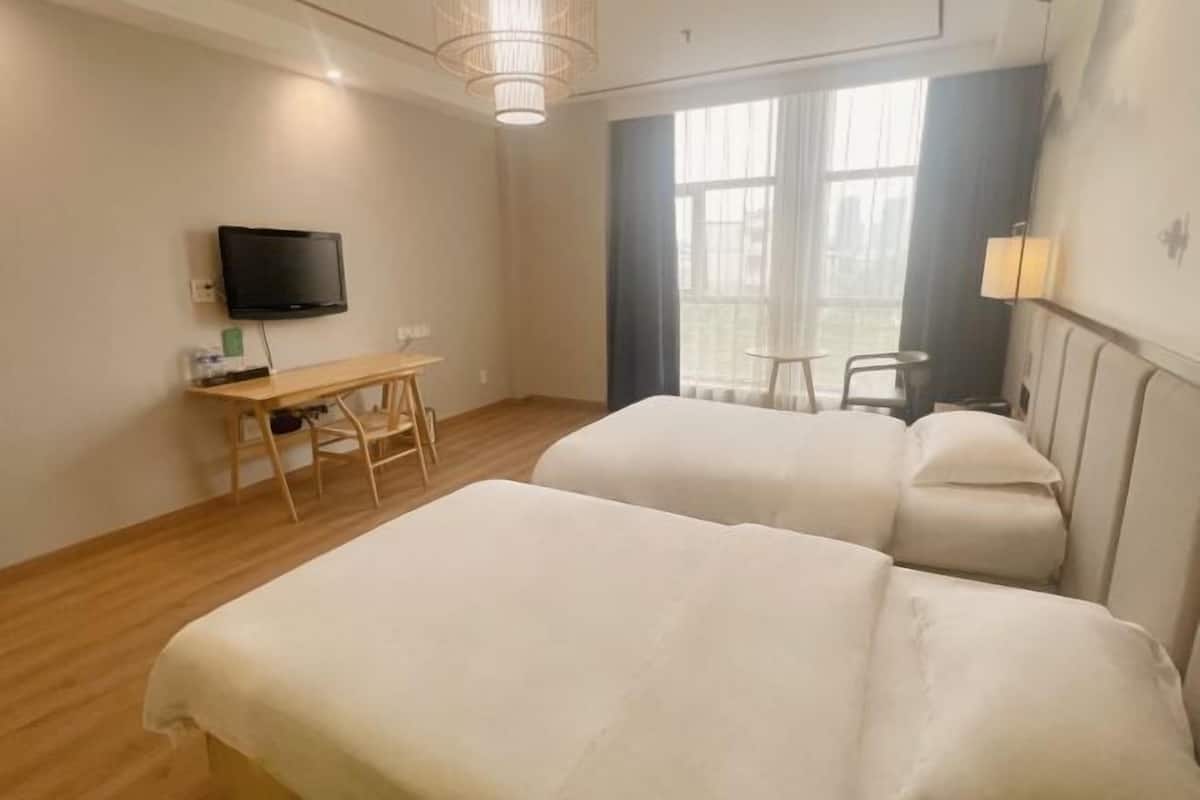 A hotel room with two beds, a desk with a chair, a television, and a window with curtains.