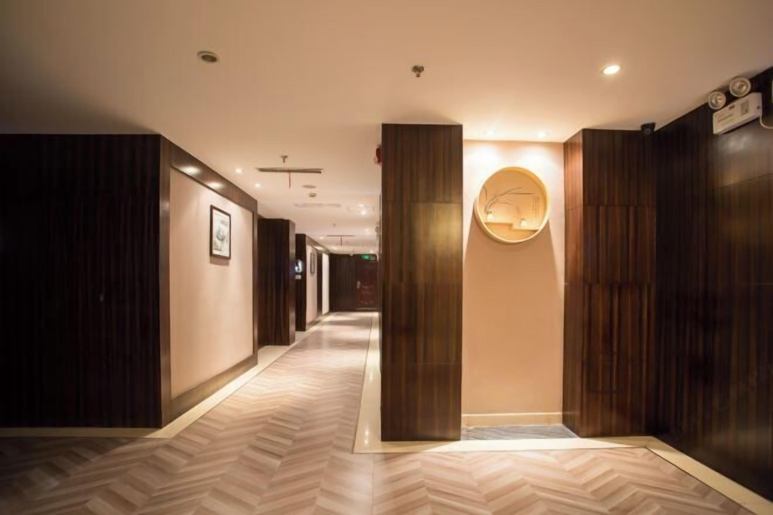 A hotel hallway with wooden paneling, a herringbone floor pattern, and a round wall-mounted light fixture.