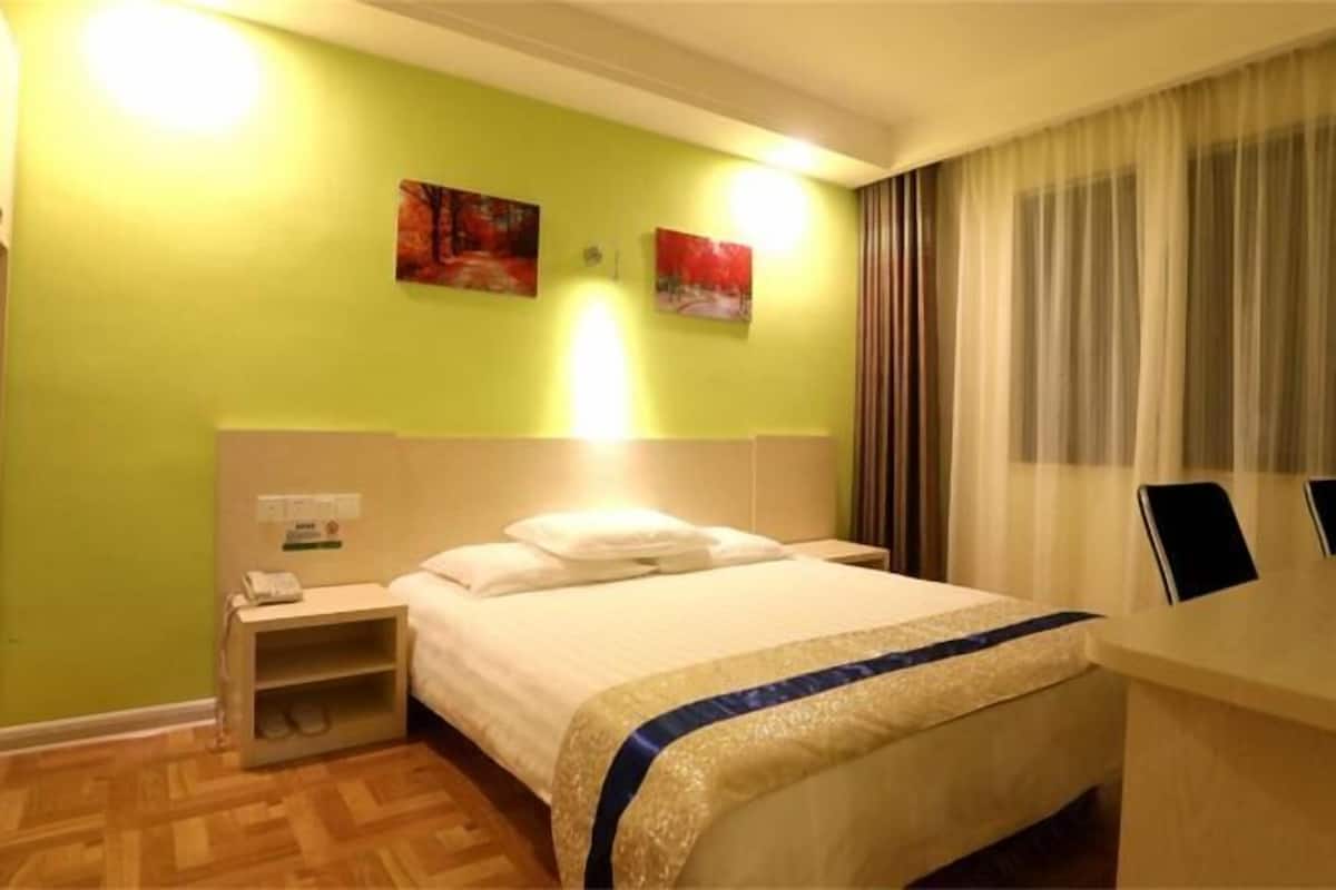 A hotel room with a bed, nightstand, and a desk with a chair.