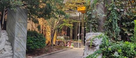 A stone pathway leading to a building entrance, surrounded by greenery and stone statues.