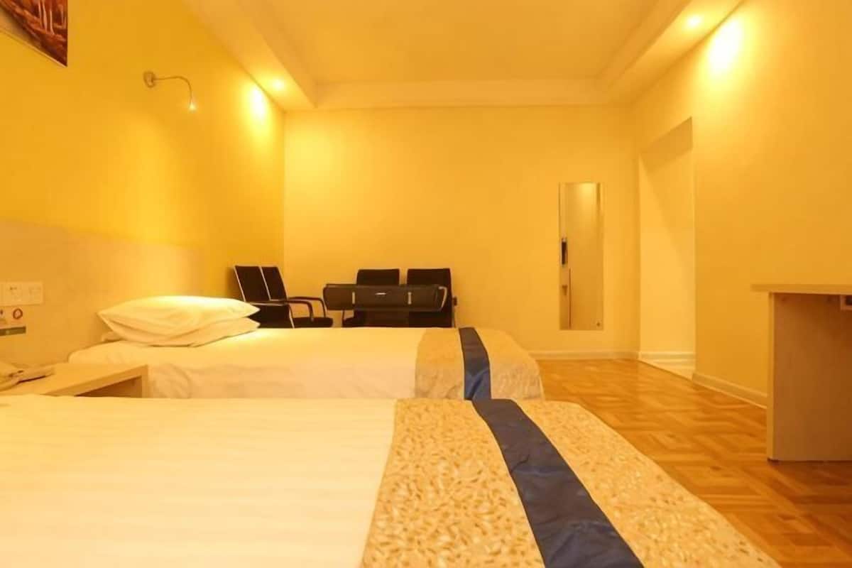 A hotel room with two beds, a desk, a chair, and a mirror.