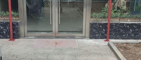 Une entrée d’immeuble avec une porte en verre, un poteau rouge et un chemin pavé de pierres.