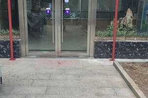 Una entrada de edificio con puerta de vidrio, un poste rojo y un camino de piedra.
