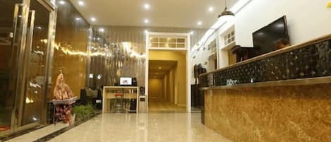 A hotel lobby with a reception desk, a glass door entrance, and a marble floor.