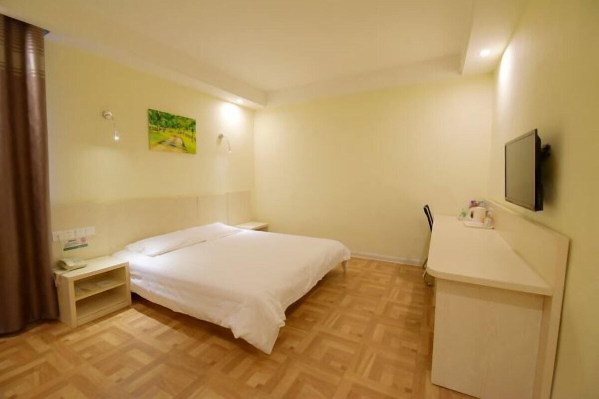 Une chambre d’hôtel comprenant un lit, une table de chevet, une petite étagère, un bureau avec une chaise, un téléviseur à écran plat et un tableau au mur.