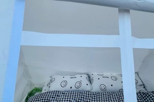 Una habitación blanca con cama, ropa de cama de cuadros y almohadones con caras sonrientes.