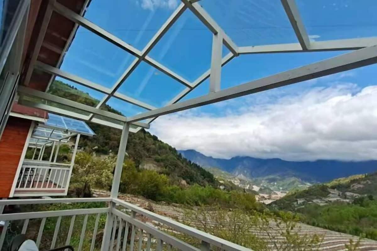 Una habitación con techo de vidrio, balcón y vista a un paisaje montañoso.