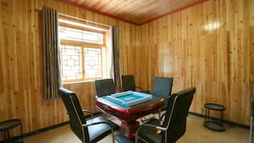 A room with a wooden paneled wall, a table with chairs, and a window with curtains.