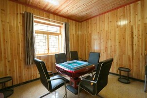 A room with a wooden paneled wall, a table with chairs, and a window with curtains.