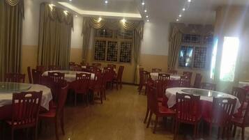 A dining area with round tables and chairs, a tiled floor, and windows with curtains.