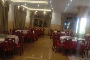 A dining area with round tables and chairs, a tiled floor, and windows with curtains.