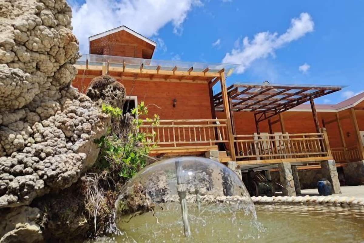 Estructura de piedra con un elemento acuático, un banco de madera y un edificio con terraza de madera.