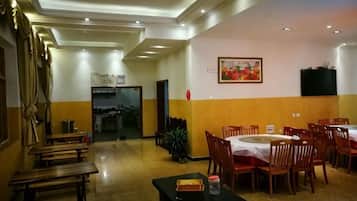 A hotel dining area with tables and chairs, a long corridor with benches, and a door leading to another room.