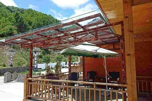 Una estructura de madera con techo de cristal, asientos al aire libre y vistas a un paisaje montañoso.