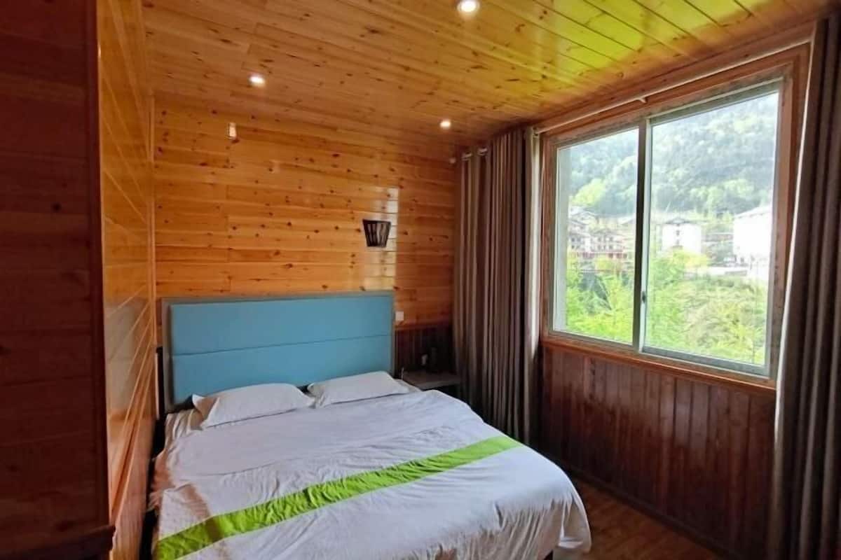 Una habitación con paneles de madera, una cama, una ventana con cortinas y una luz nocturna en la pared.