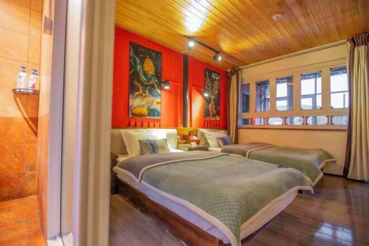 A room with two beds, wooden ceiling, red walls, and a window with curtains.