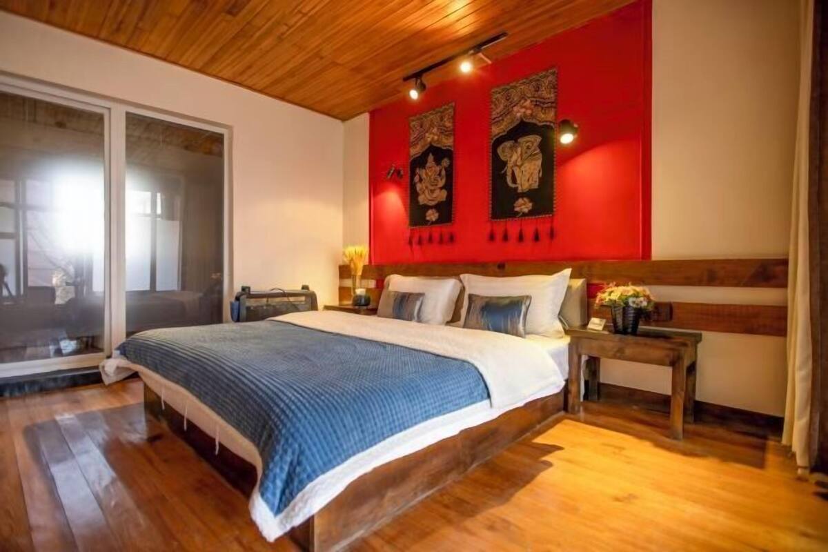 A bedroom with a large bed, wooden flooring, a red accent wall, and a sliding glass door.