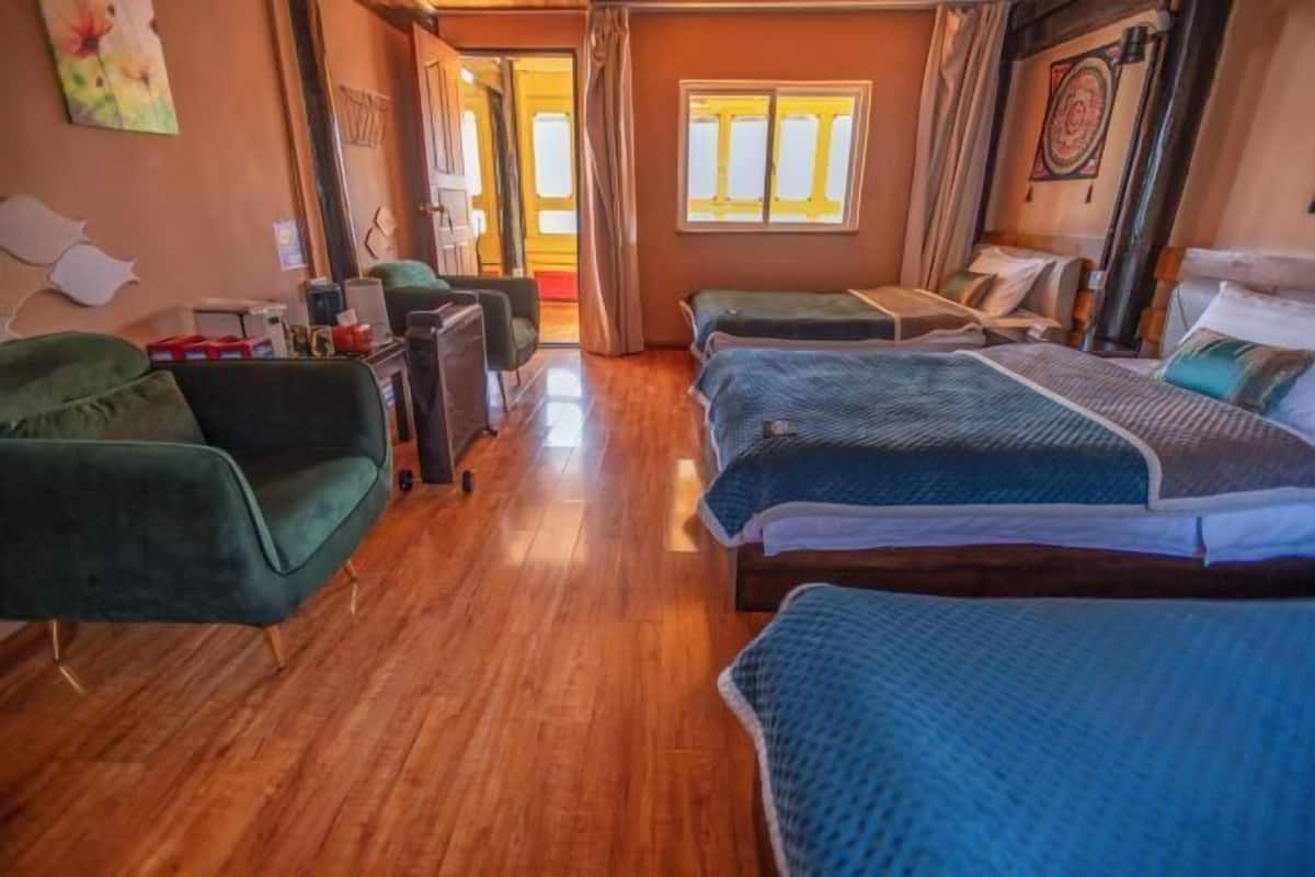 A room with wooden flooring, two beds with blue bedding, a green sofa, a desk, and a chair.