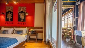 A bedroom with a wooden floor, a bed with pillows, a nightstand, and a window with curtains. - Cozy Mountain Inn (Shangri-La)