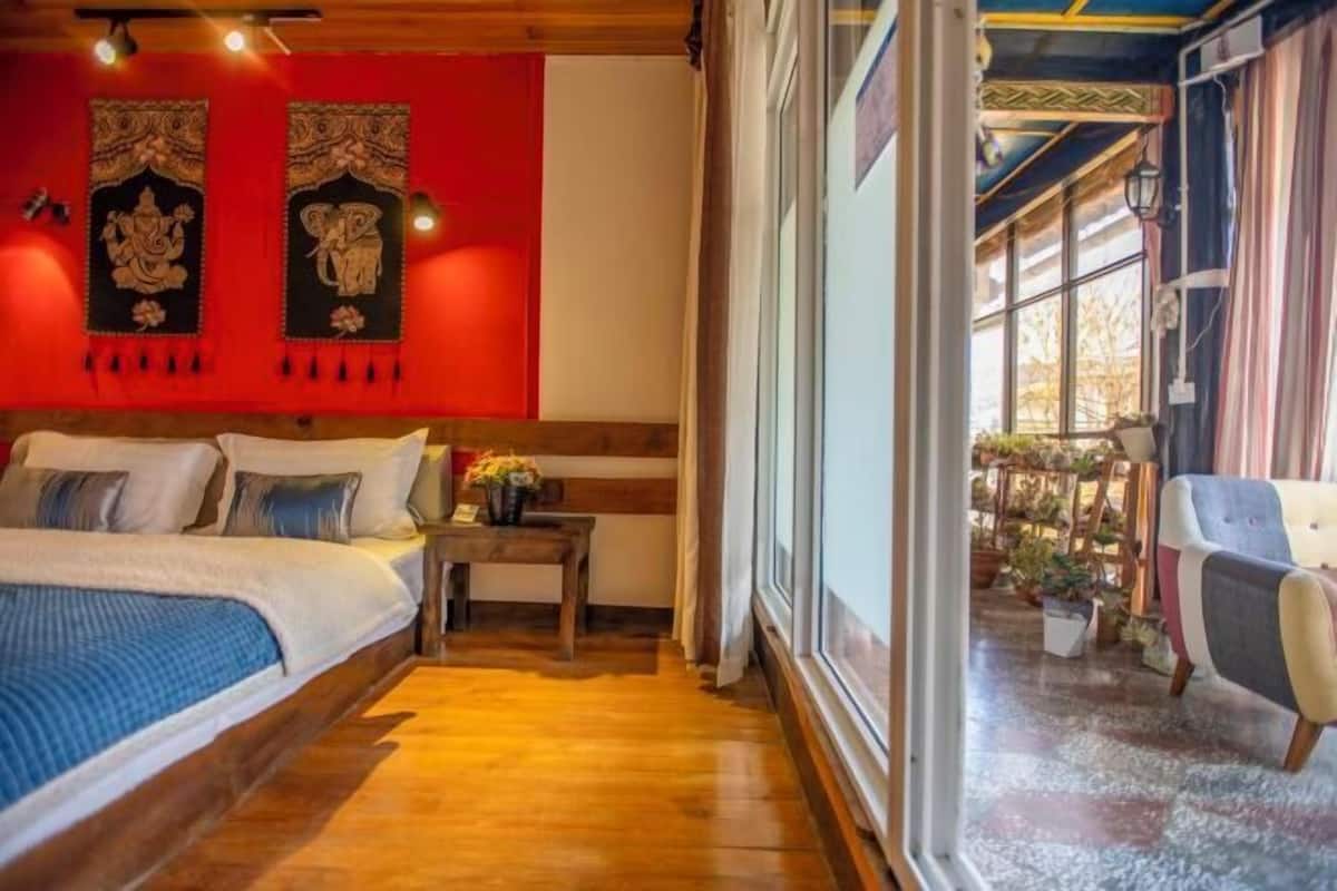 A bedroom with a wooden floor, a bed with pillows, a nightstand, and a window with curtains.