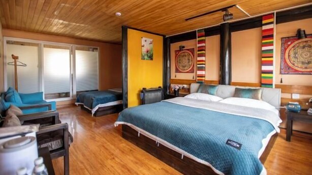 A bedroom with a large bed, a wooden ceiling, and a sliding glass door leading to a balcony. - Cozy Mountain Inn (Shangri-La)