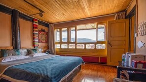 A room with a wooden ceiling, a large bed with a blue blanket, a window with a view, and a door. - Cozy Mountain Inn (Shangri-La)