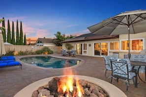 Un jardin avec une piscine, un foyer extérieur, du mobilier de jardin et une terrasse couverte.