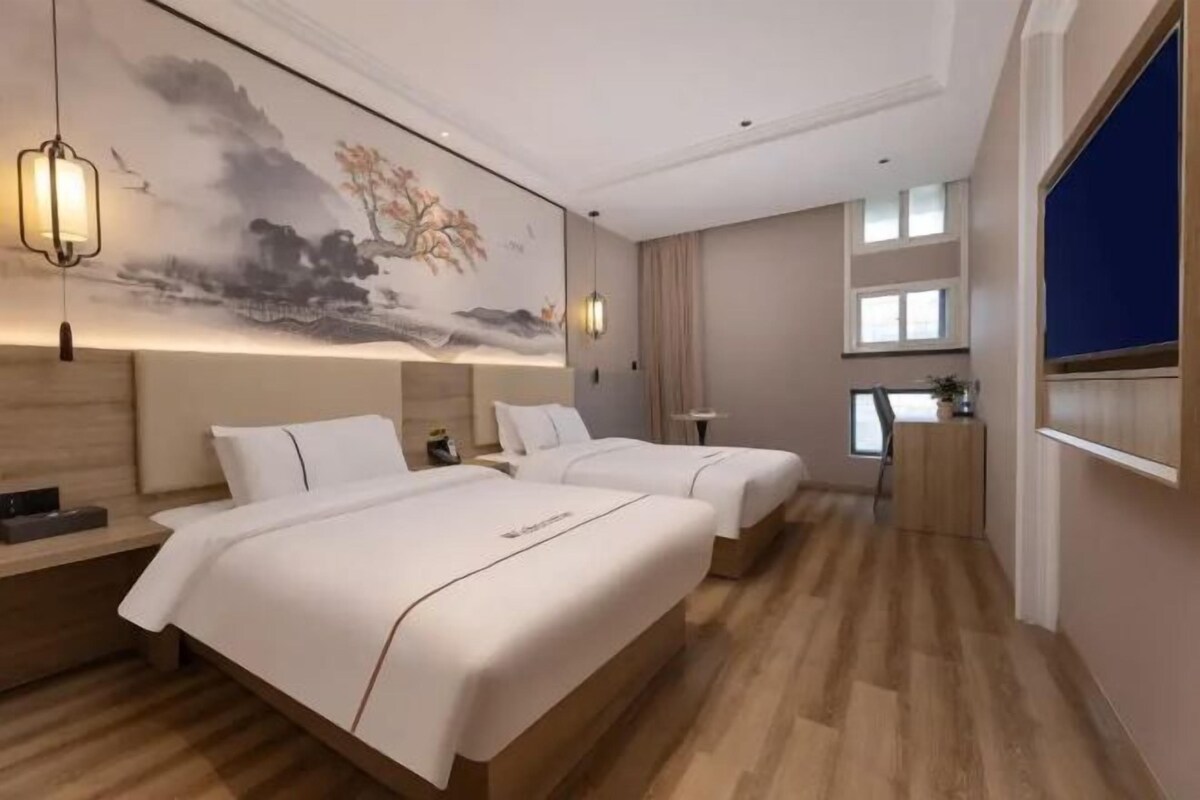 Habitación de hotel con dos camas, una obra de arte grande en la pared y un escritorio con una computadora.