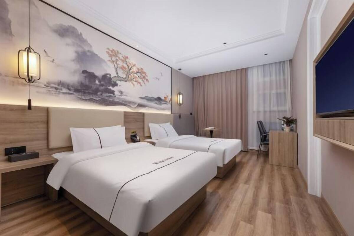 A hotel room with two beds, a desk, a chair, and a large painting on the wall.