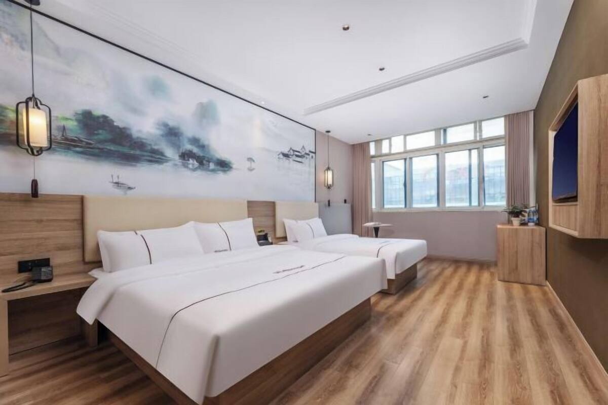 A hotel room with a large bed, a smaller bed, a desk, and a large window.