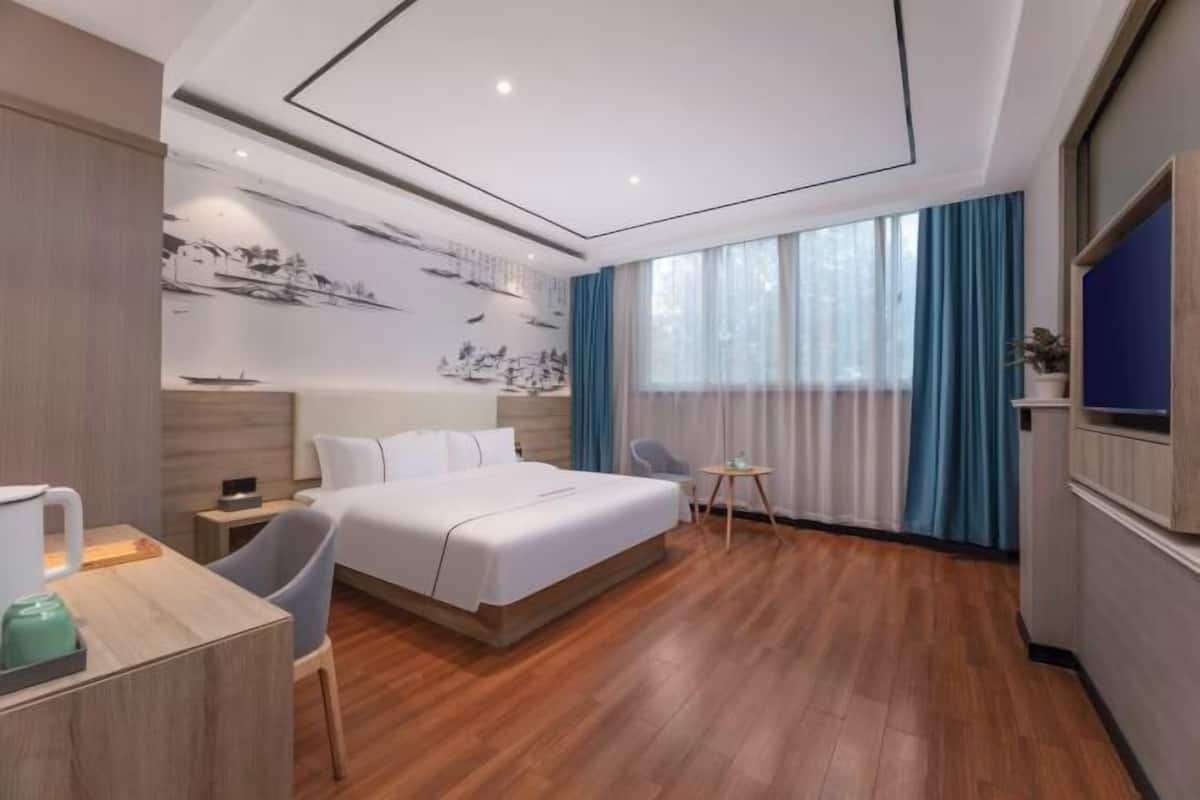 A modern hotel room with a large bed, a desk with a chair, a small table, and a TV mounted on the wall.