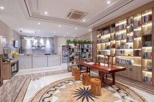 Un moderno vestíbulo de hotel con una recepción, una amplia estantería, un área de comedor y una alfombra decorativa.