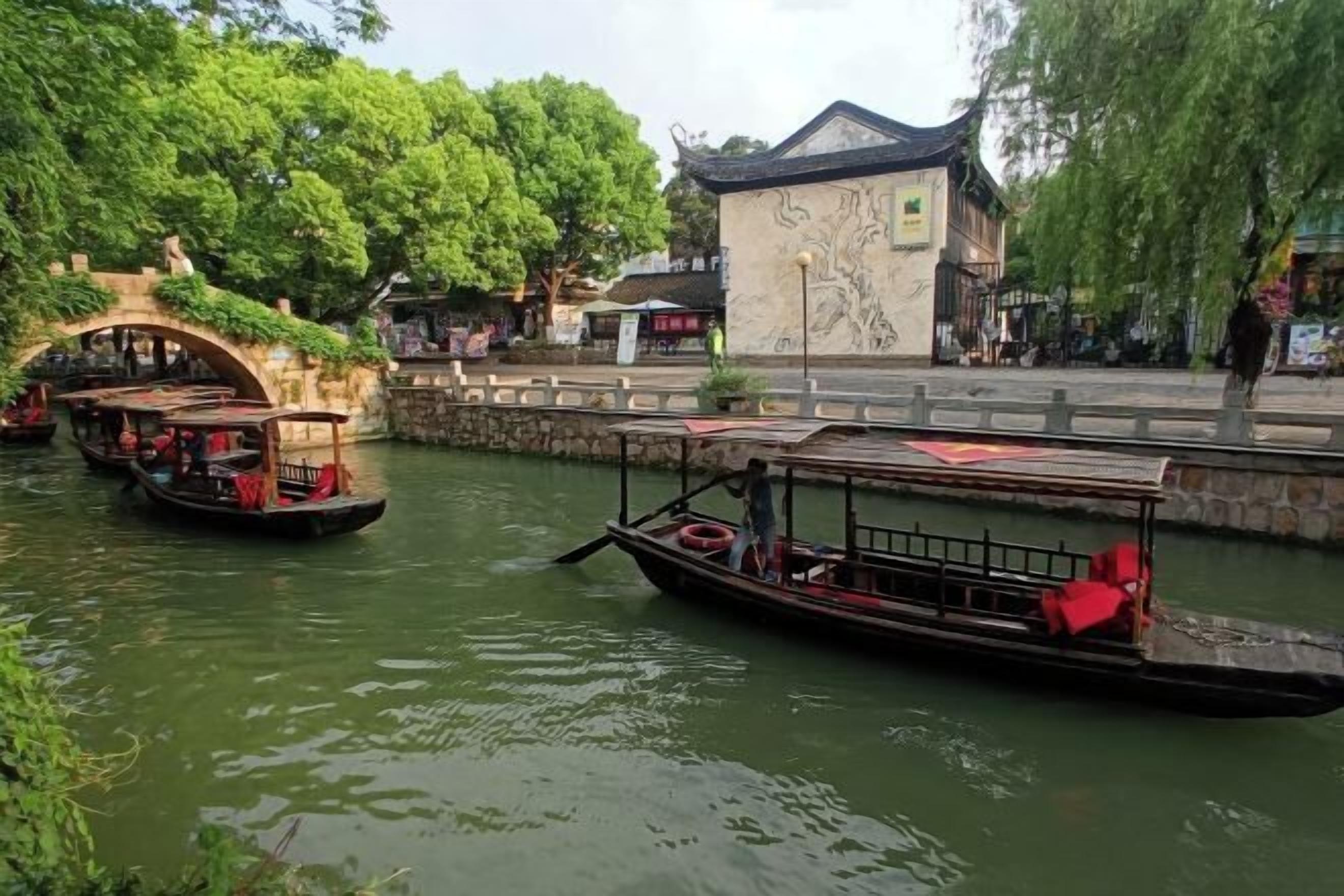 A traditional wooden boat on a river, with stone bridges and buildings in the background.