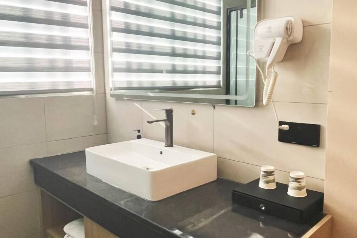 A modern bathroom with a white sink, a black countertop, a hair dryer, and a mirror.