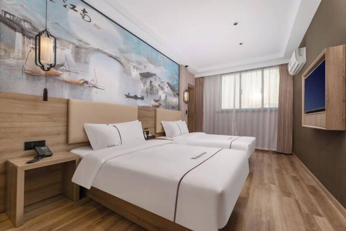 A hotel room with two beds, a large painting on the wall, a wooden floor, and a TV mounted on the wall.