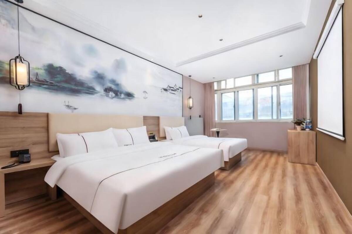 A modern hotel room with a large bed, bedside tables, a painting on the wall, and a large window.