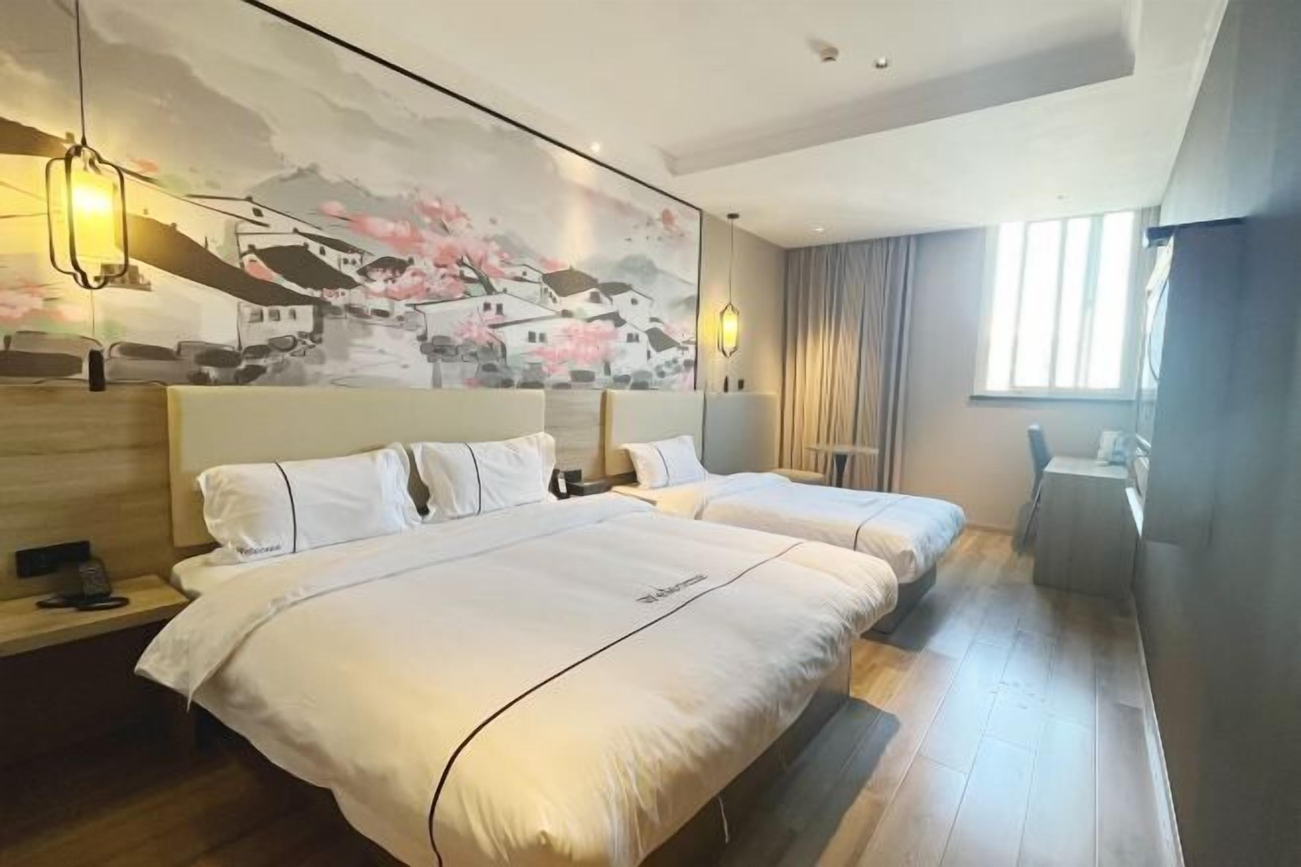 A hotel room with two beds, a mural on the wall, a desk, and a window.