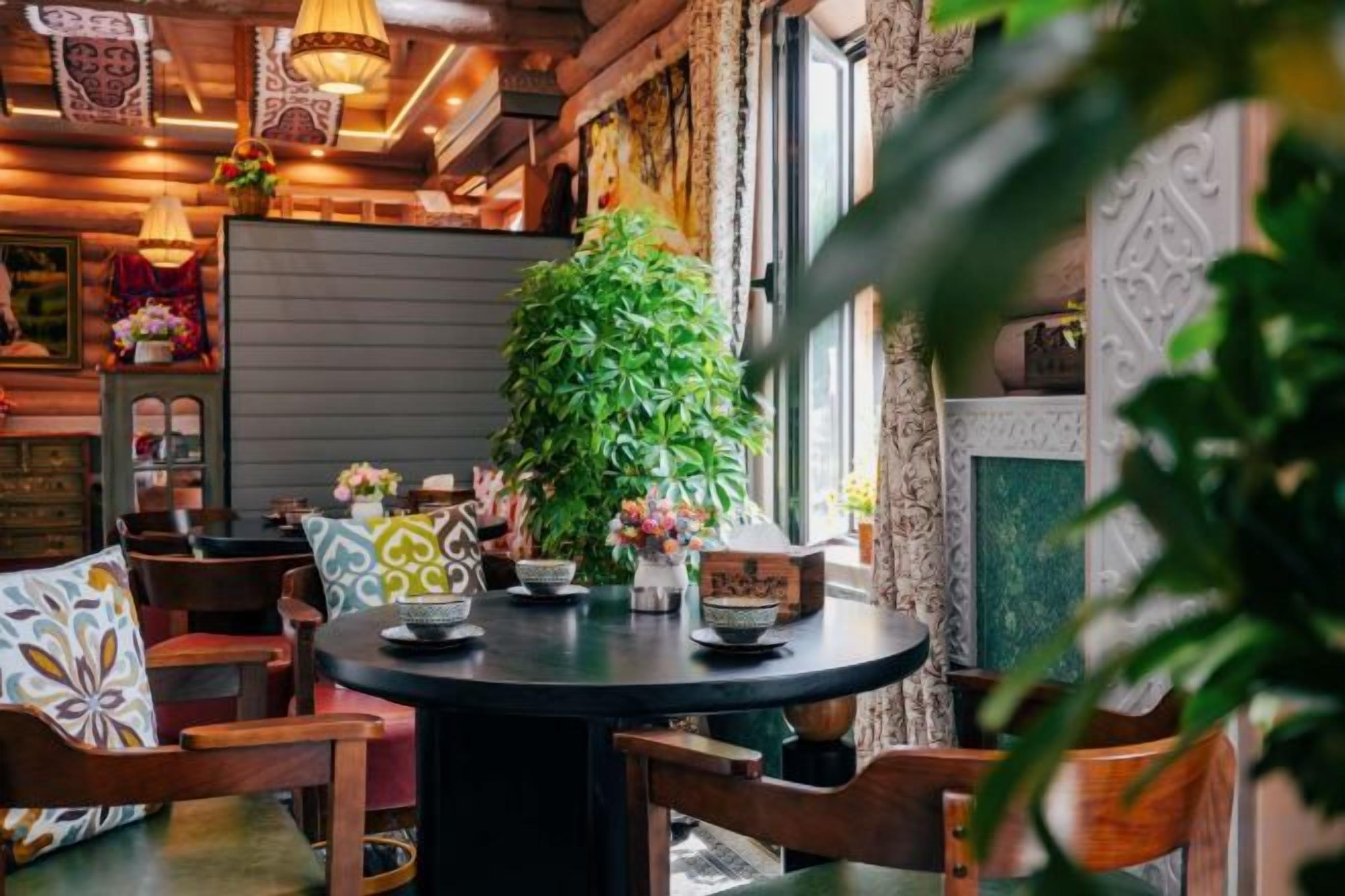 Una mesa redonda con sillas, una planta en maceta y elementos decorativos en una habitación con muebles de madera y un papel tapiz estampado.