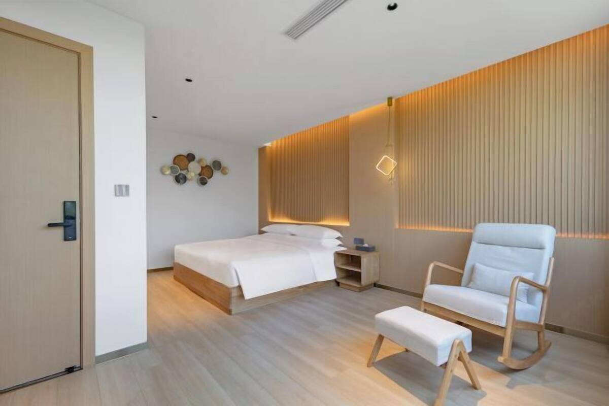 A modern bedroom with a bed, bedside tables, a rocking chair, and a bench.