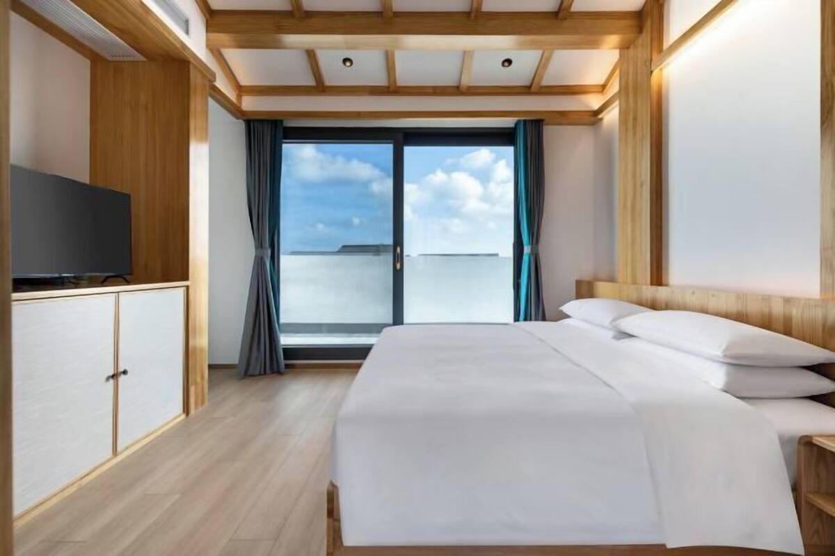 A hotel room with a bed, a TV, a wardrobe, and a view of the sea.