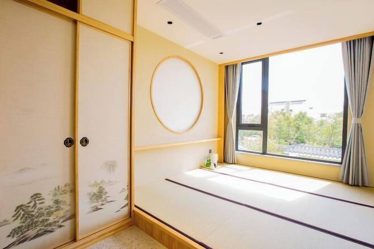 A tatami mat room with a sliding door, a window with curtains, and a wall-mounted circular decoration.