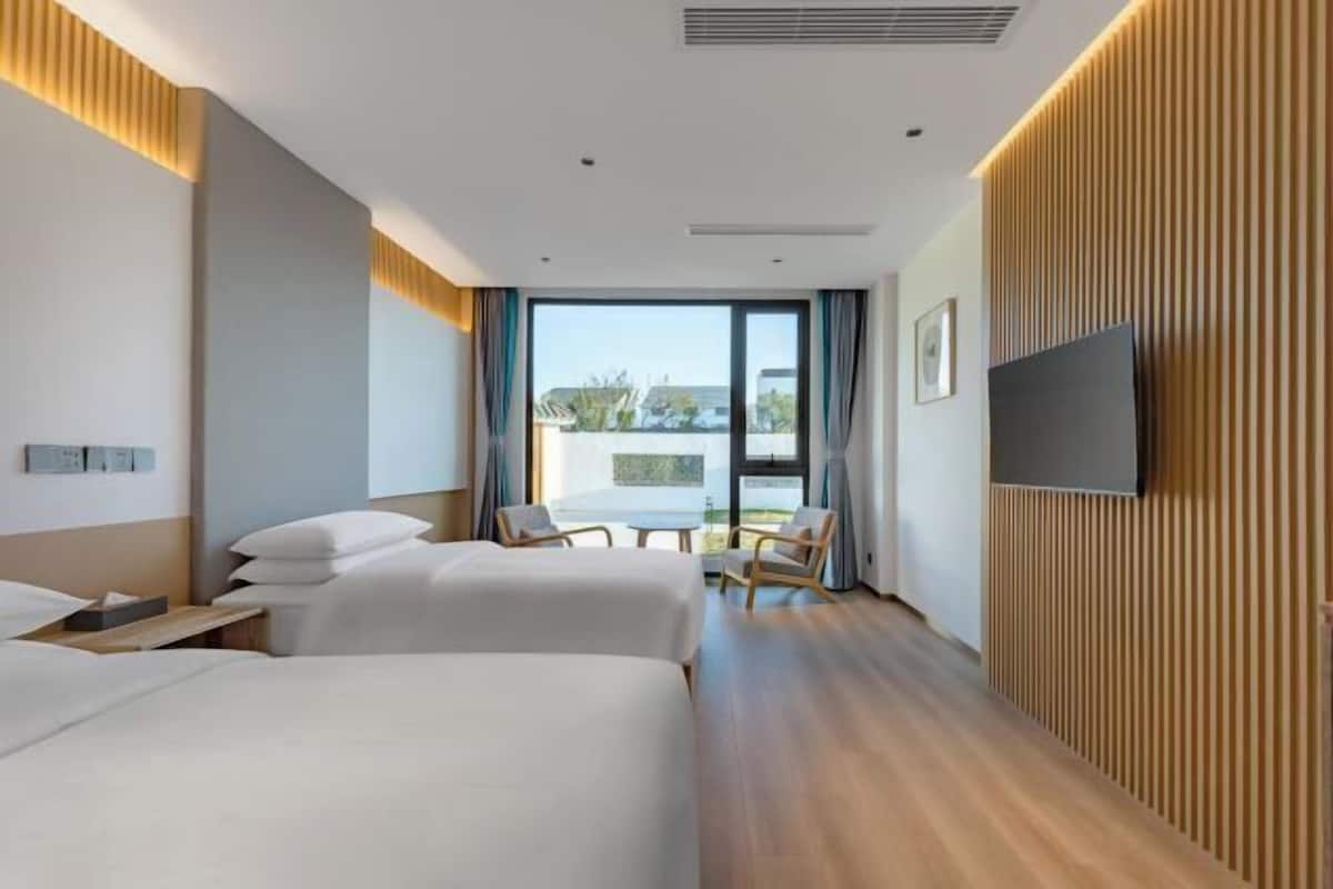 A hotel room with two beds, a TV, a dining table with chairs, and a view of the outdoors.