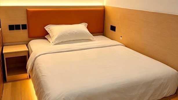 Ein Einzelbett mit Kopfteil, ein Nachttisch und eine Wandleuchte.