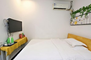 A hotel room with a bed, a flat-screen TV, an air conditioner, a small table with a kettle, a cup, and a box of tissues. - Style Theme Hotel (Fuyang Normal University West Lake Campus) (Fuyang)