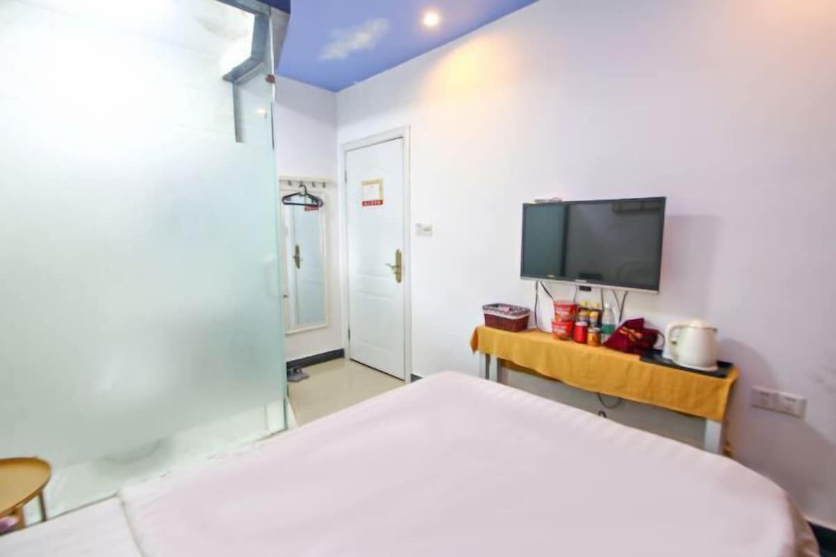 A hotel room with a bed, a television on a stand, a small table with toiletries, and a door leading to another room.
