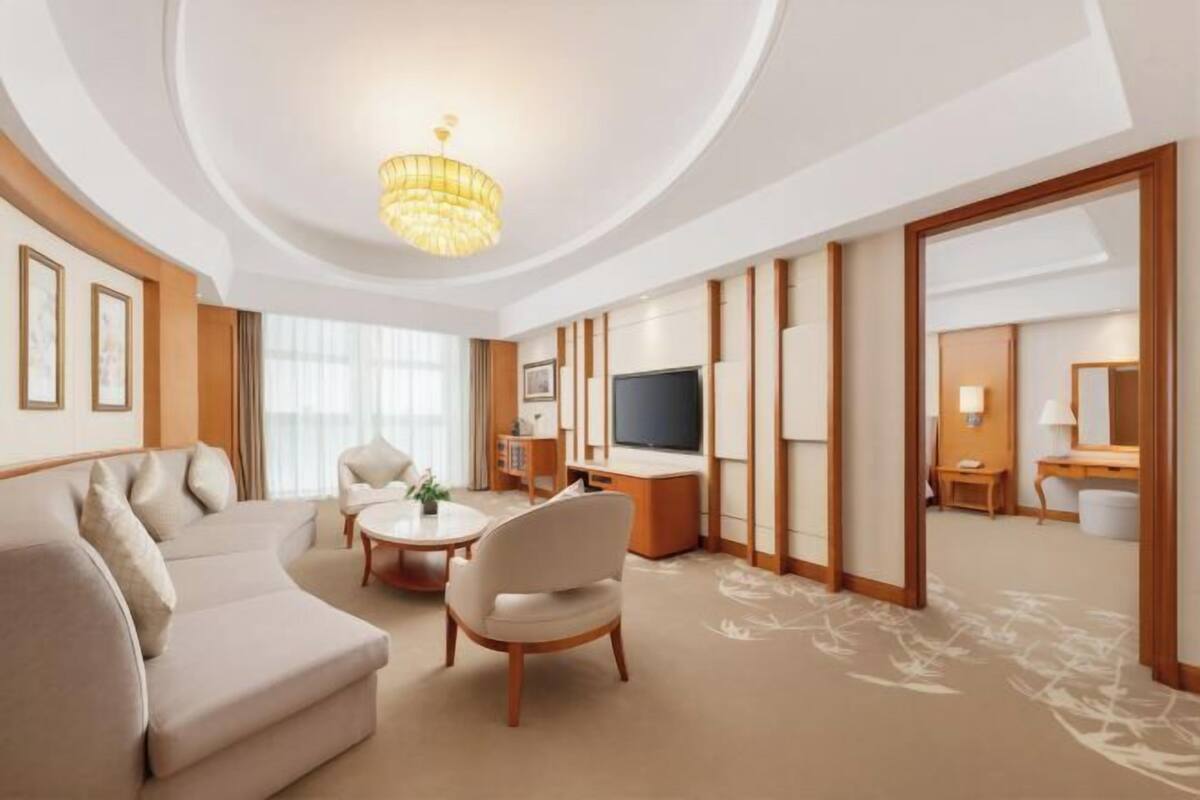 Una habitación de hotel moderna con techo curvo, una araña, un sofá, una silla, un escritorio con televisor de pantalla plana y un espejo grande.