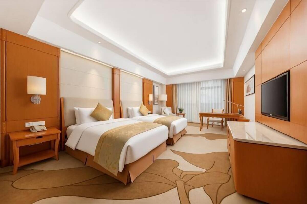 Habitación de hotel con dos camas, un escritorio, un televisor y un ventanal grande.