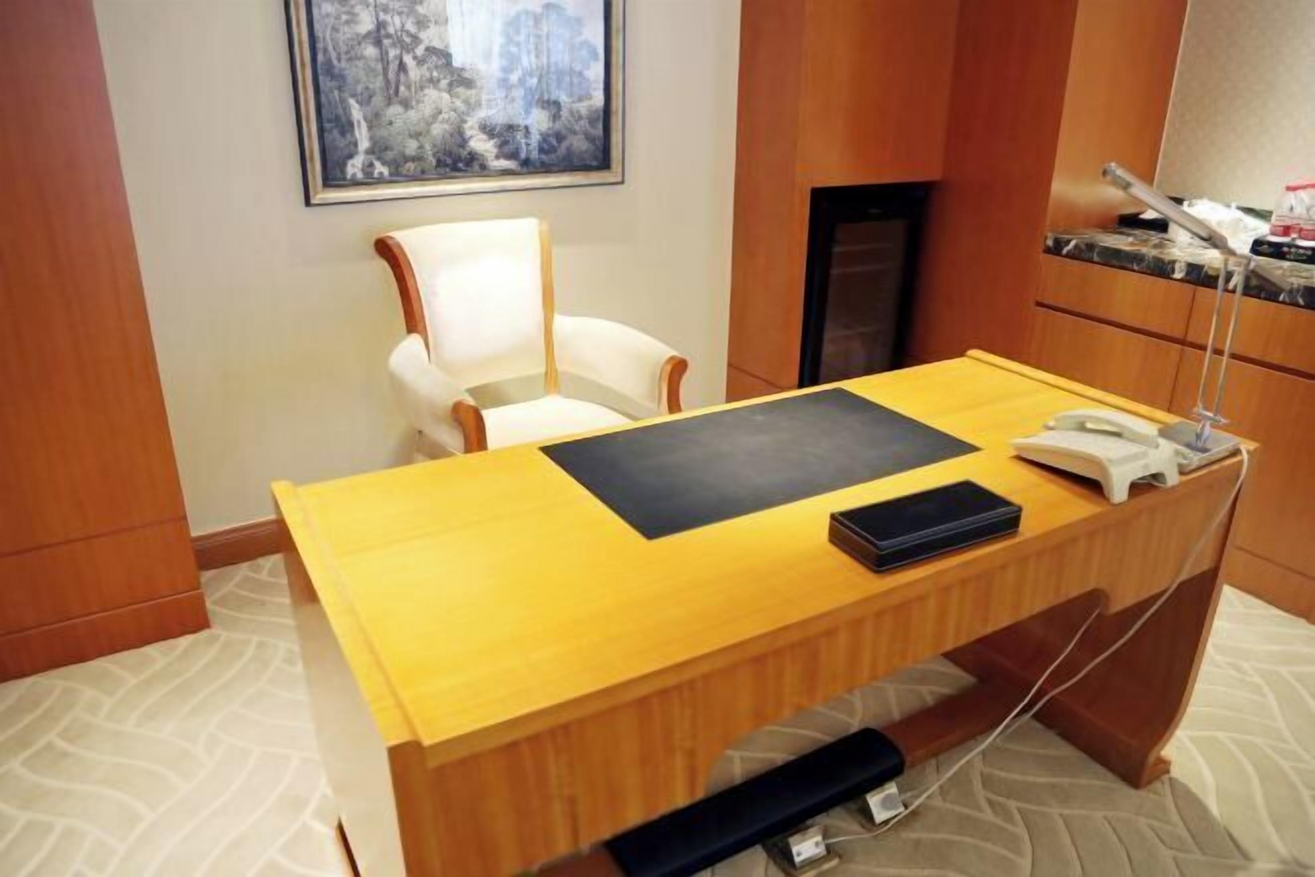 A hotel room with a wooden desk, a chair, a telephone, and a framed picture on the wall.