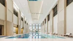 Une vaste piscine intérieure à l’eau claire, entourée de hauts plafonds et de grandes fenêtres.
