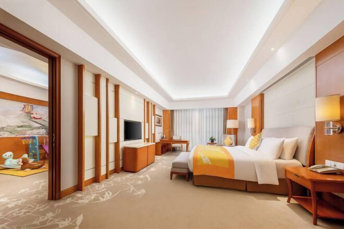 Habitación de hotel con cama, mesitas de noche, televisor, escritorio y ventana con cortinas.